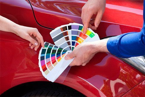 Un hombre y una mujer miran una paleta de colores en un coche rojo.