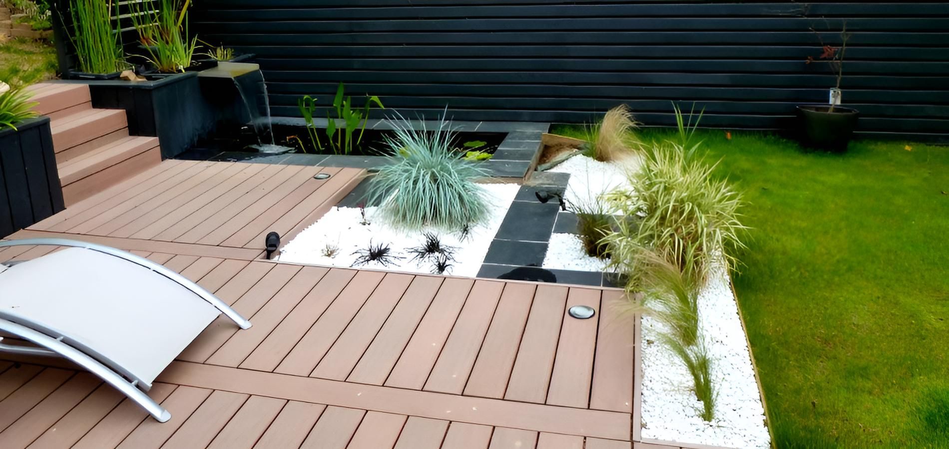 Un patio moderne avec une terrasse en bois marron, un petit bassin décoratif, des parterres de gravier blanc, des graminées ornementales et une chaise longue.
