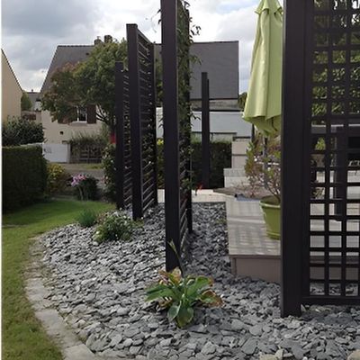 Un élément de jardin moderne composé de panneaux d'intimité en bois noir au-dessus d'un parterre en pierre grise, situé à côté d'une terrasse en bois.