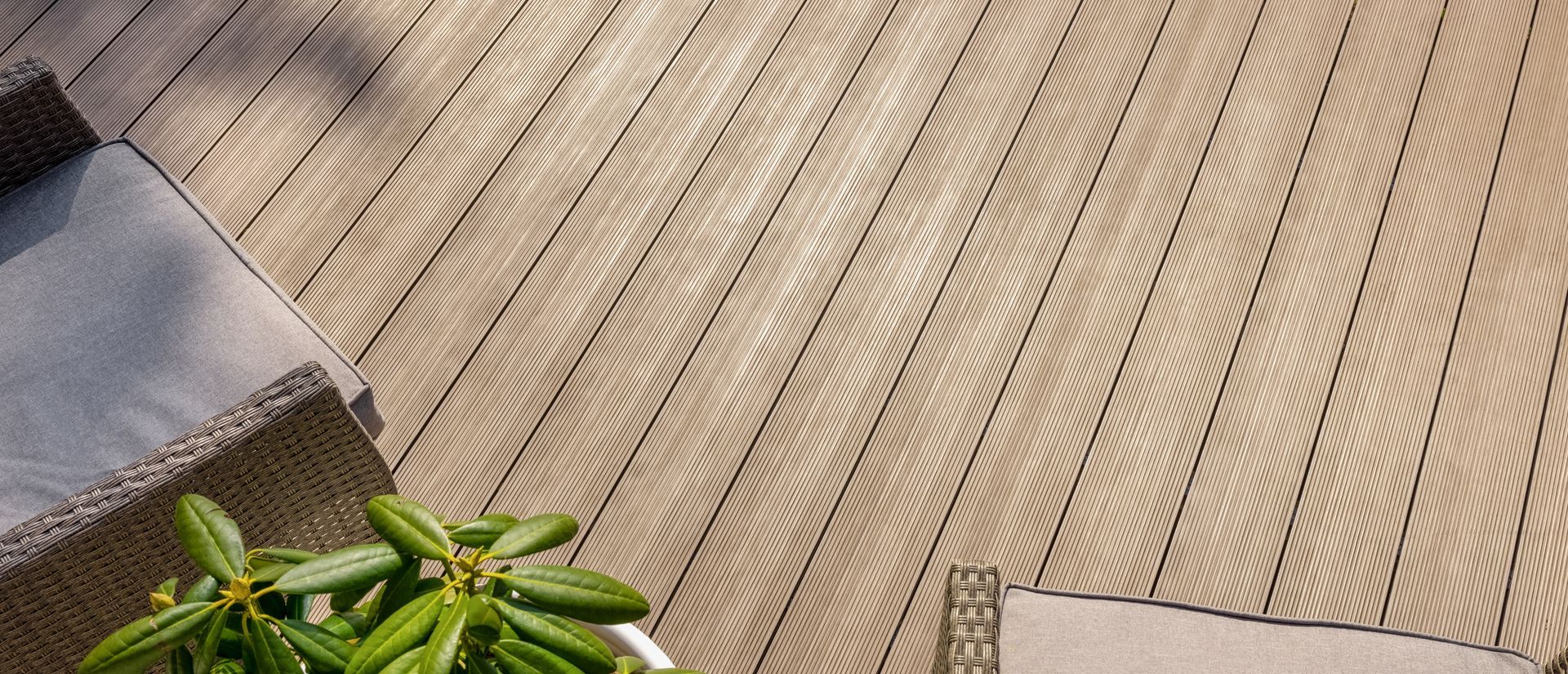 Un tapis d'extérieur neutre à motifs, posé sur une terrasse en bois, partiellement recouverte par des chaises longues et une plante en pot.