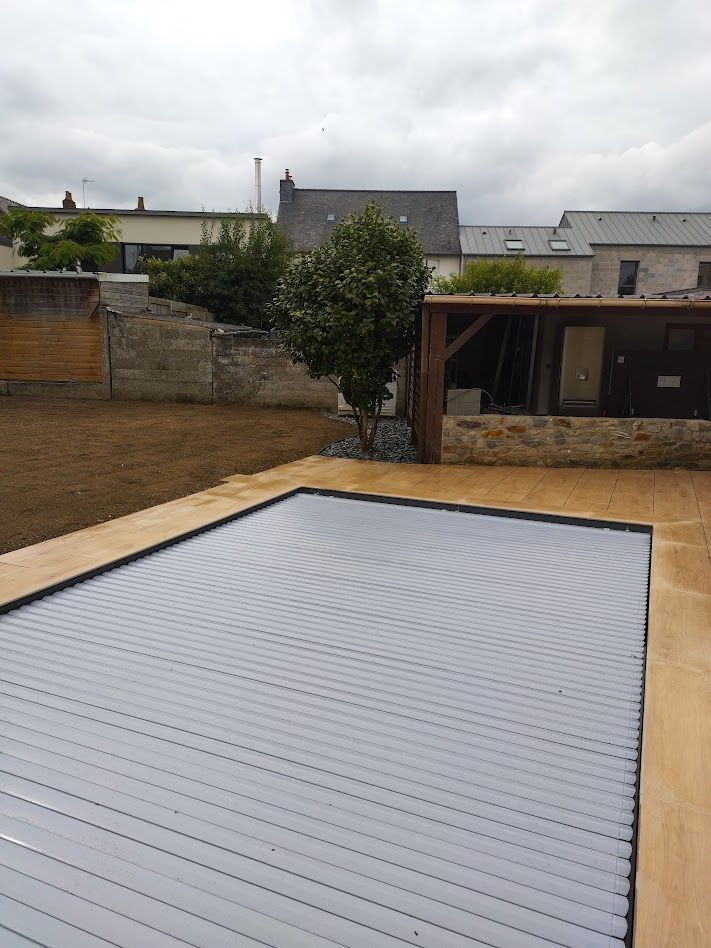 Terrasse arrière avec piscine couverte, terrasse en bois, clôture et arbres sous un ciel couvert