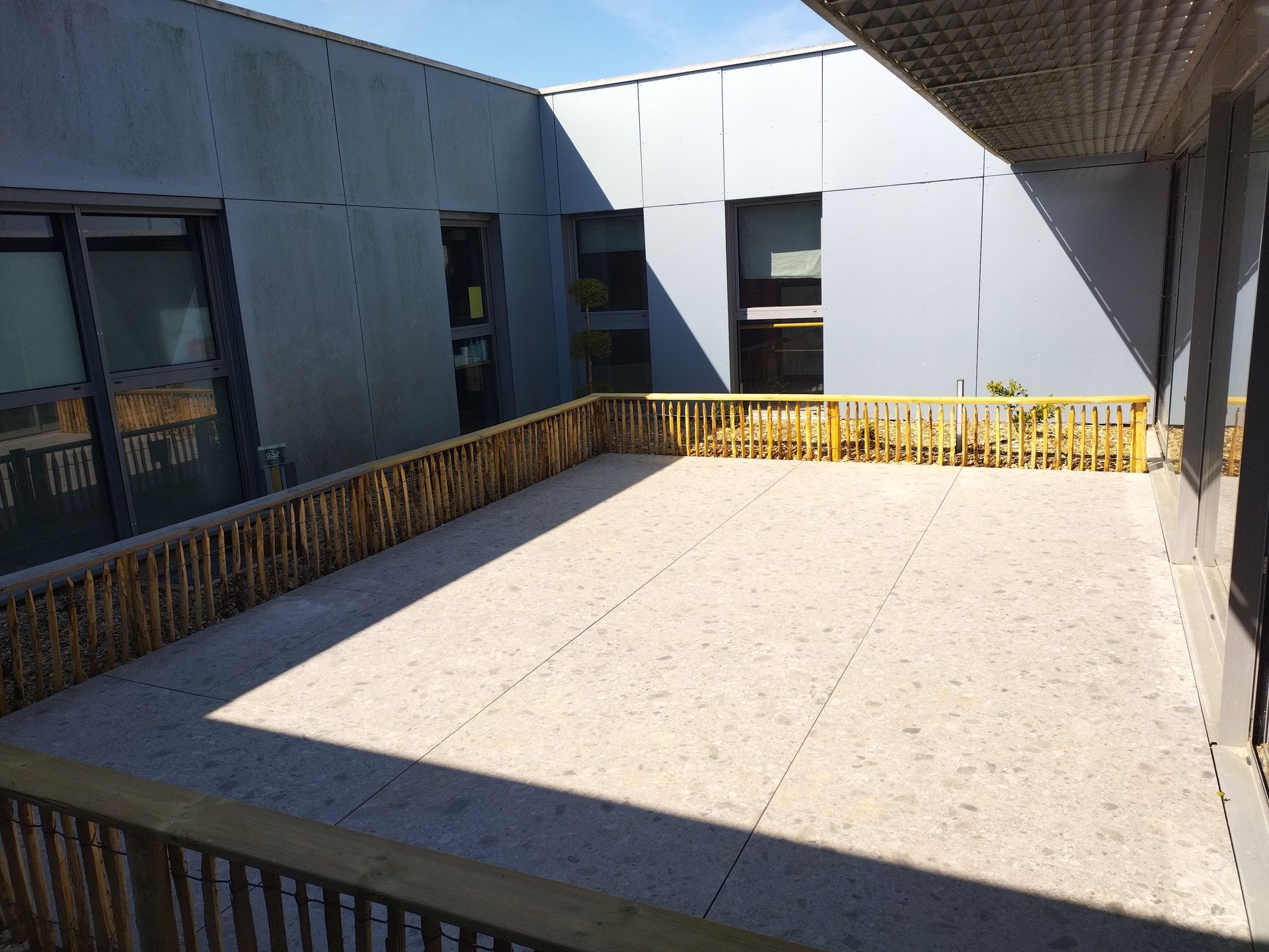 Cour intérieure vide, avec des murs en béton et une balustrade jaune, baignée de soleil.