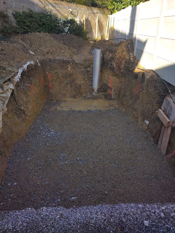 Zone de fondation excavée dans la cour arrière avec base de gravier, murs de soutènement et tuyau de drainage blanc.