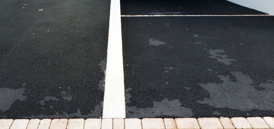 Vue aérienne de deux places de parking en asphalte foncé séparées par une ligne blanche, avec des pavés clairs à leur base.