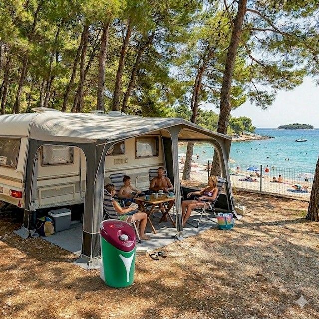 Une tente de camping sur une plage ombragée, avec des gens assis à l'intérieur, la mer bleue et des nageurs en arrière-plan.