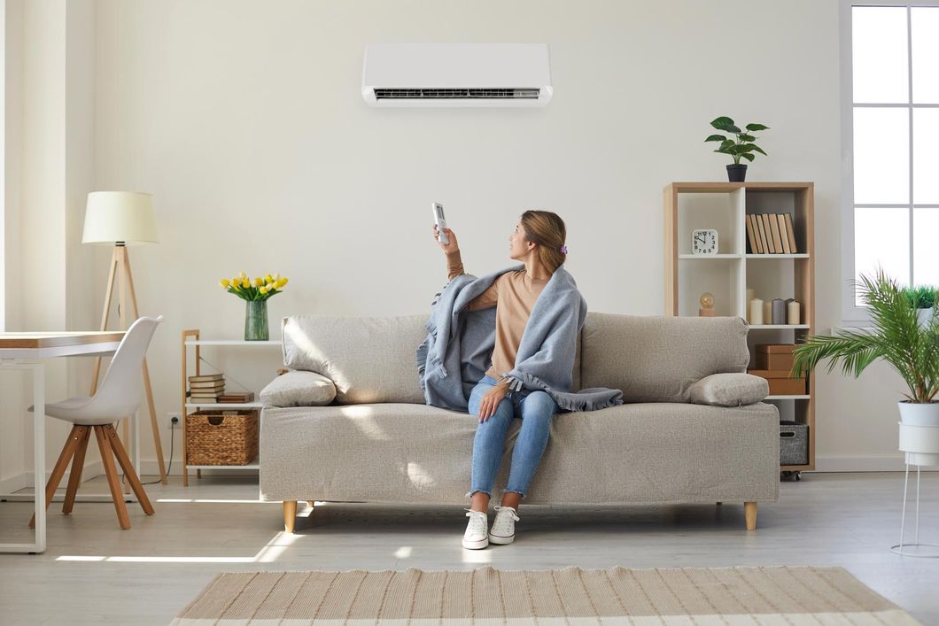 Une jeune femme assise dans un canapé visant un climatiseur avec une télécommande