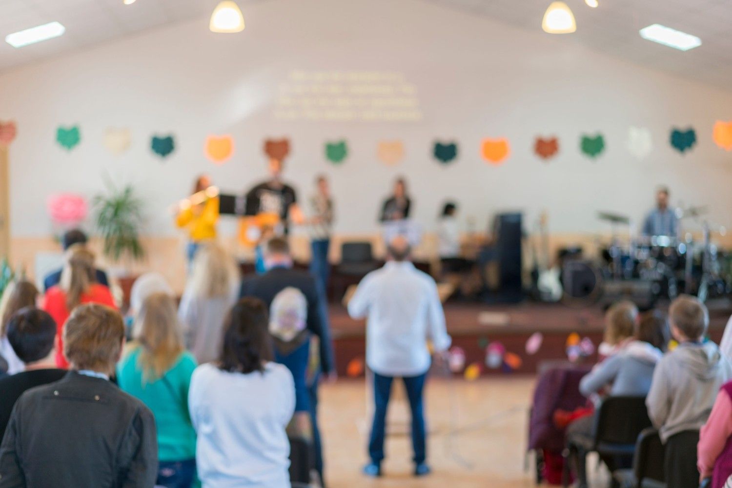 Imagen borrosa de un grupo de personas frente a un escenario durante una actuación en una sala grande.