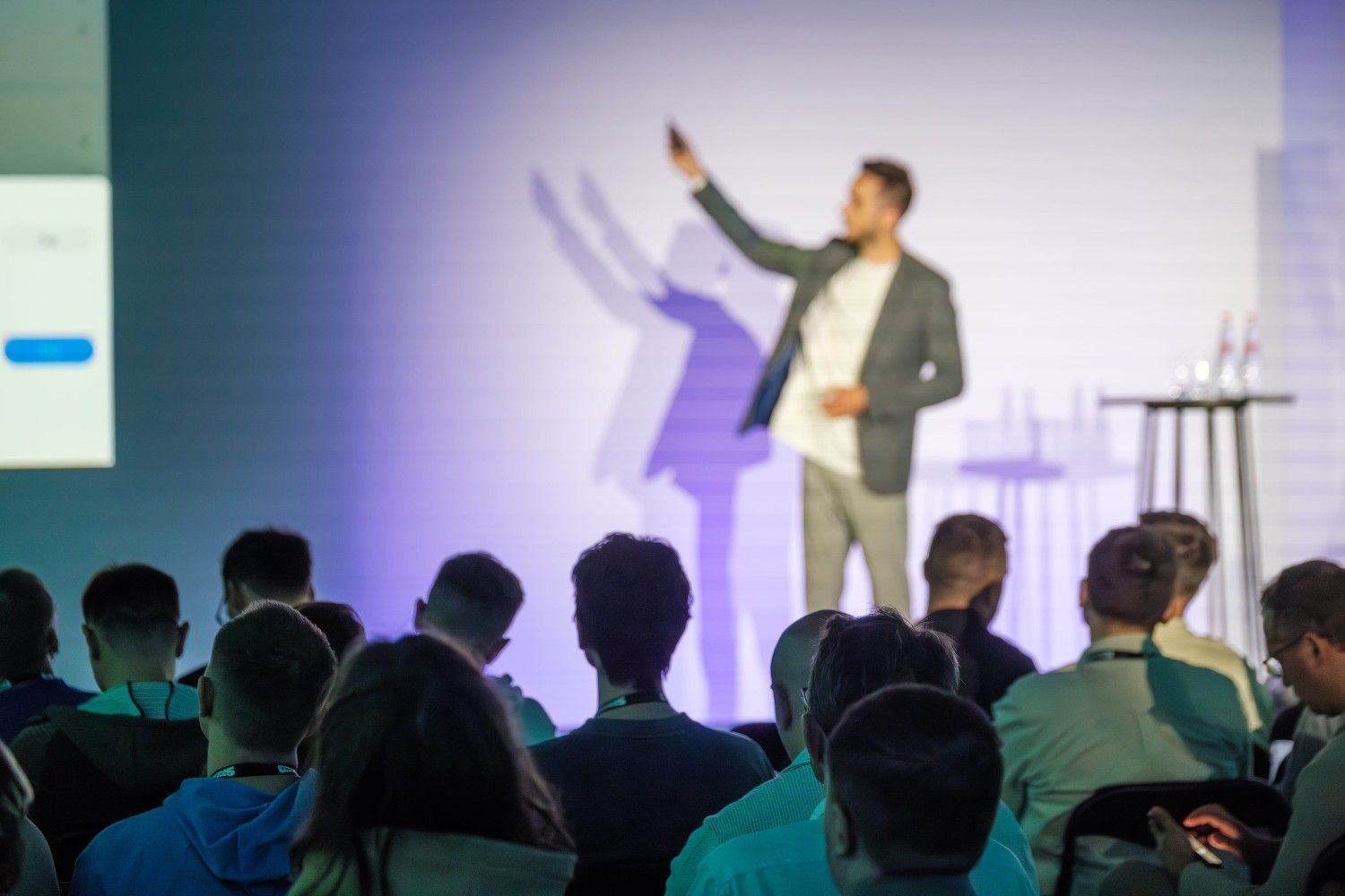 Un orador señala una pantalla mientras se dirige a una audiencia en un aula de conferencias.