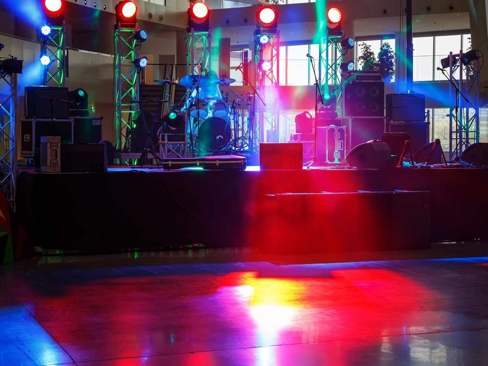 Montaje del escenario con instrumentos musicales, equipos de audio y luces de escenario de colores rojo, azul.