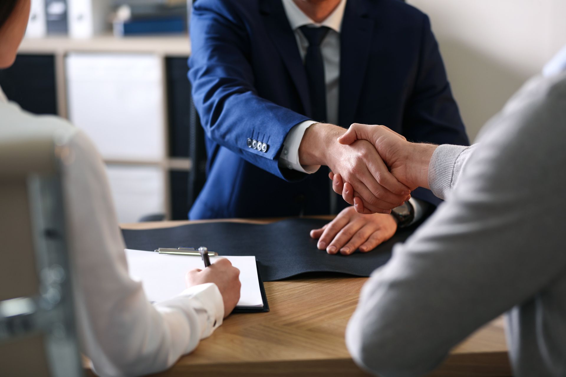 Personne signant un formulaire pendant que deux autres personnes se serrent la main