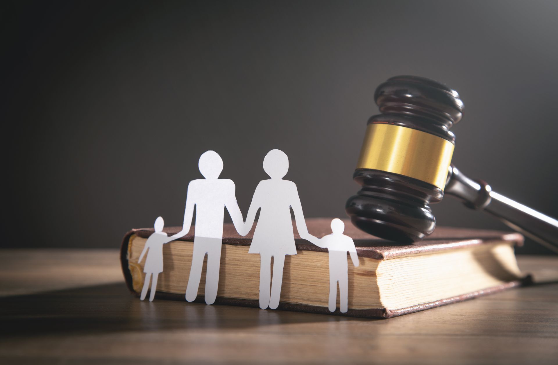 Silhouette d'une famille en papier posée devant un livre et un maillet de justice