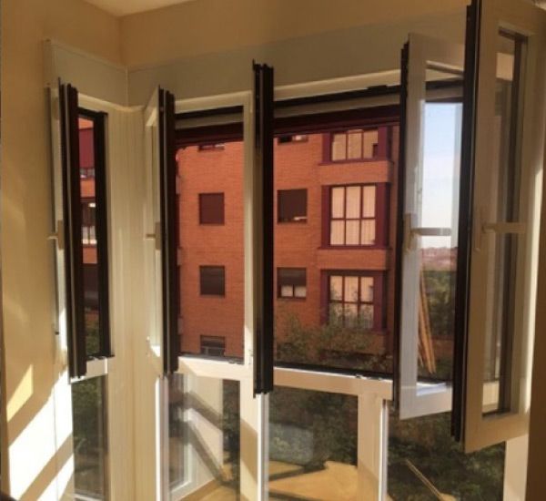 Una habitación con muchas ventanas abiertas y un edificio al fondo.