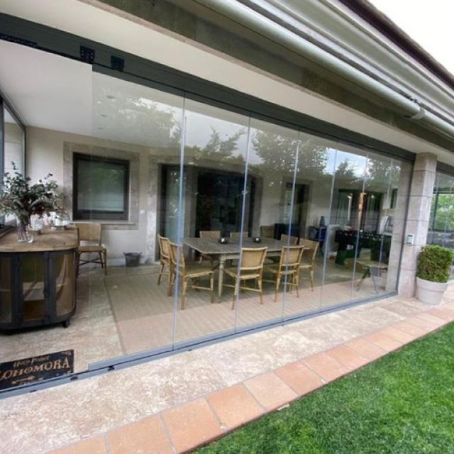 Un patio con una mesa y sillas detrás de una pared de vidrio.