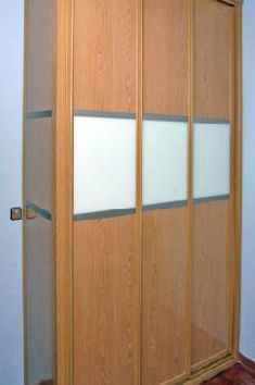 Un armario de madera con puertas corredizas de cristal en un dormitorio.