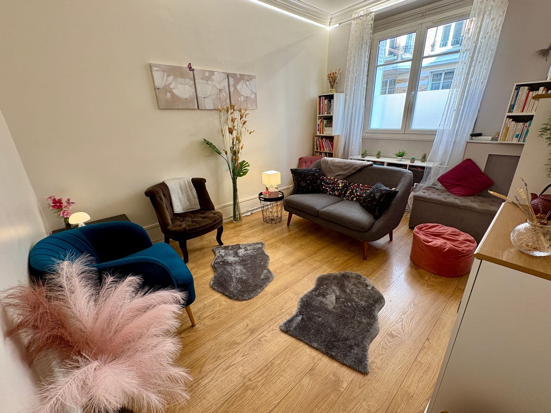 Une pièce confortable et ensoleillée avec parquet, meublée d'un canapé gris, de fauteuils foncés, de tapis moelleux et d'éléments décoratifs.