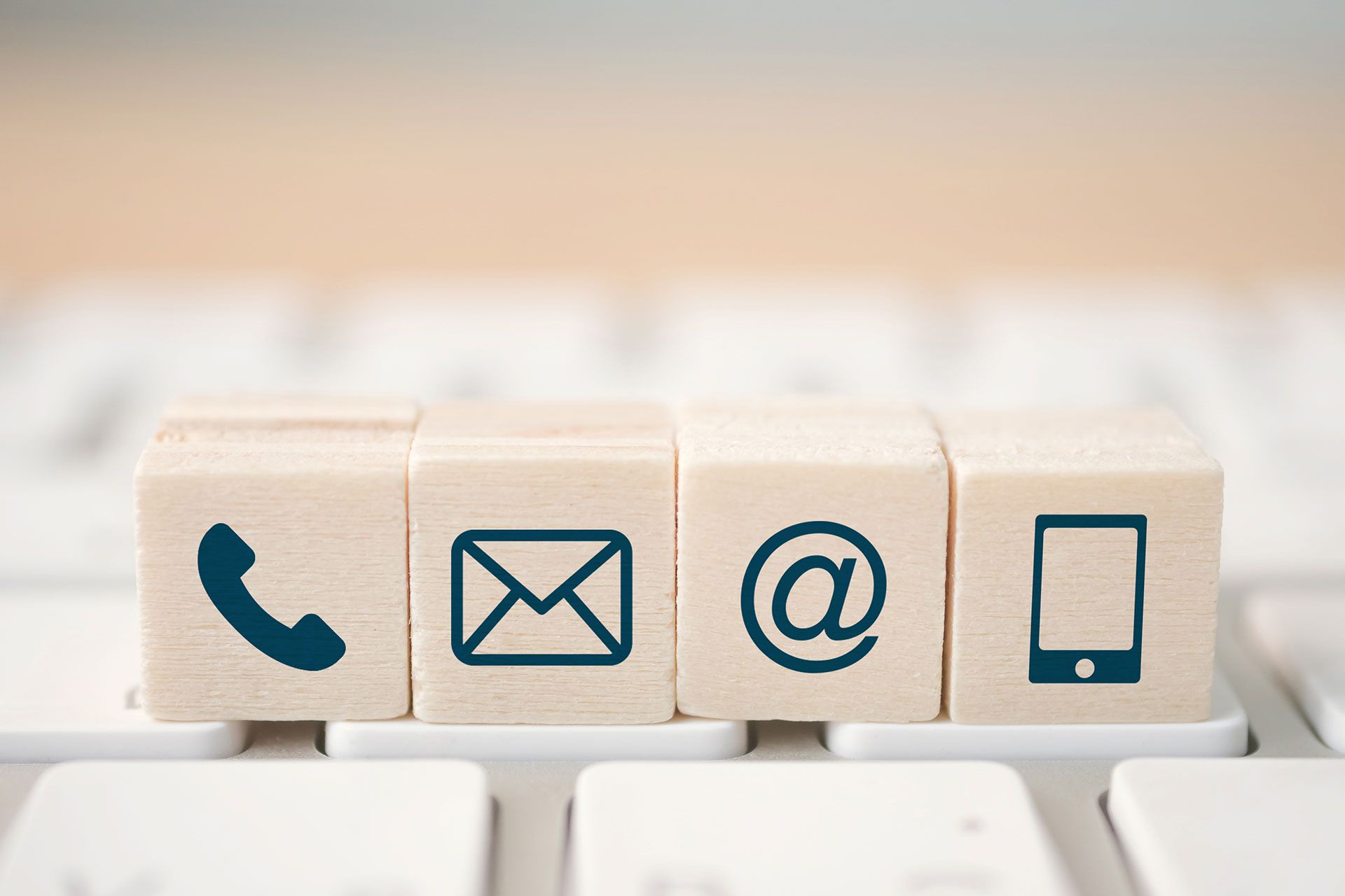 Ein Holzblock mit Telefon-, E-Mail- und Mobiltelefonsymbolen auf einer Tastatur.