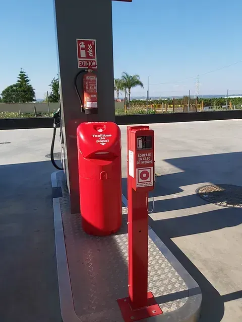 Una gasolinera con un bote de basura rojo y un extintor de incendios