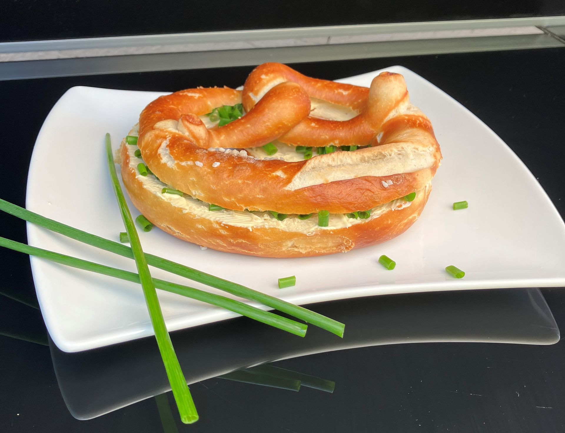 Eine Brezel auf einem weißen Teller mit Frühlingszwiebeln