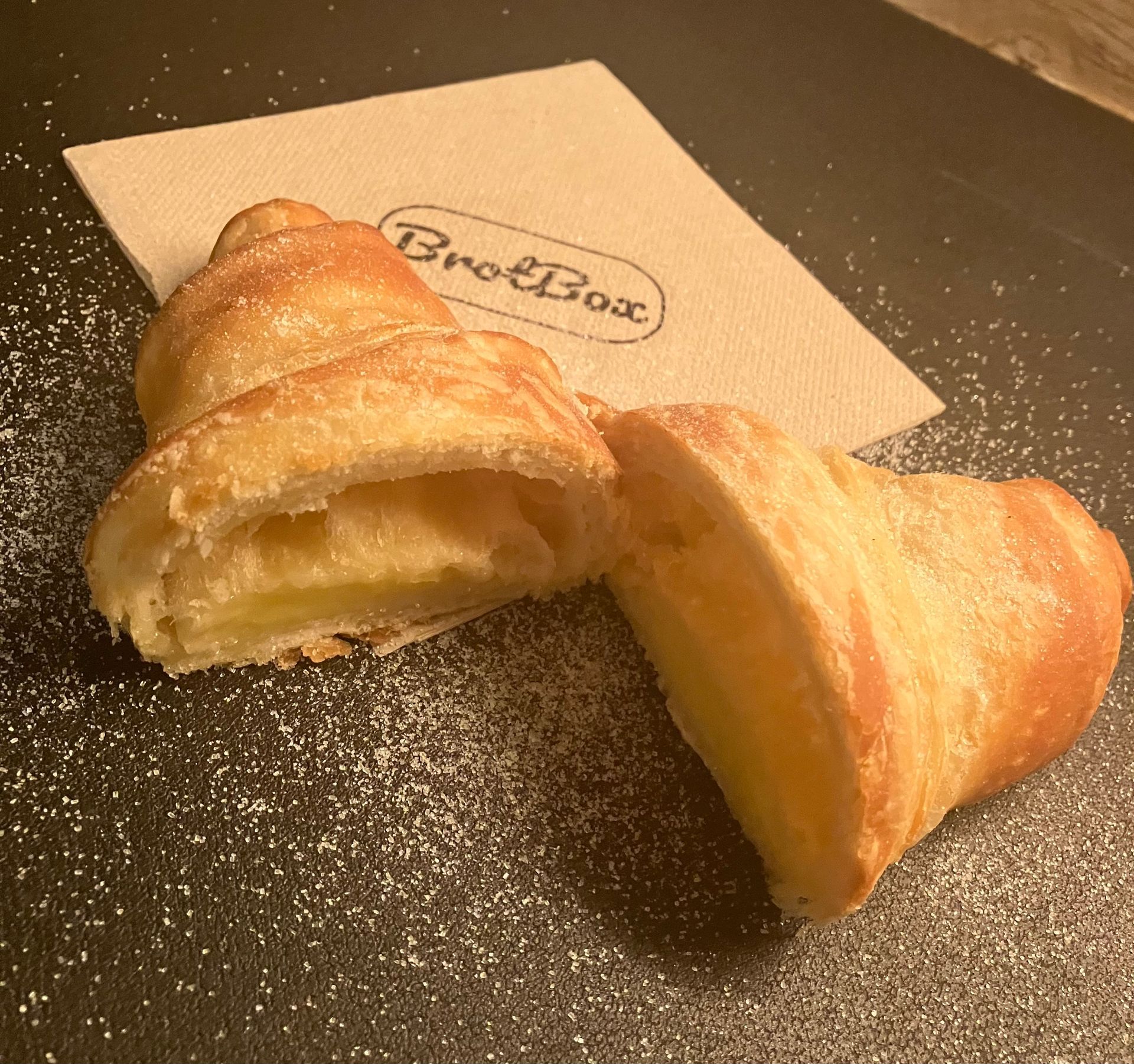 Ein Croissant wird in zwei Hälften geschnitten, neben einer Serviette mit der Aufschrift „Breadbox“