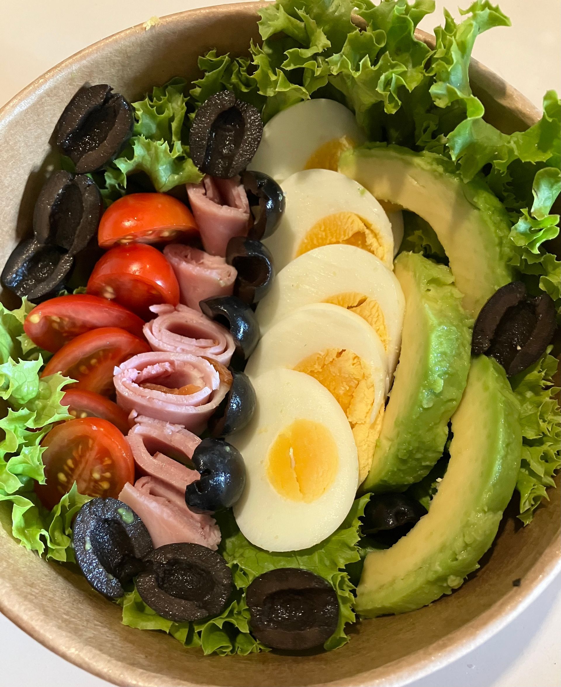 Ein Salat mit Eiern Avocado Tomaten Oliven und Schinken