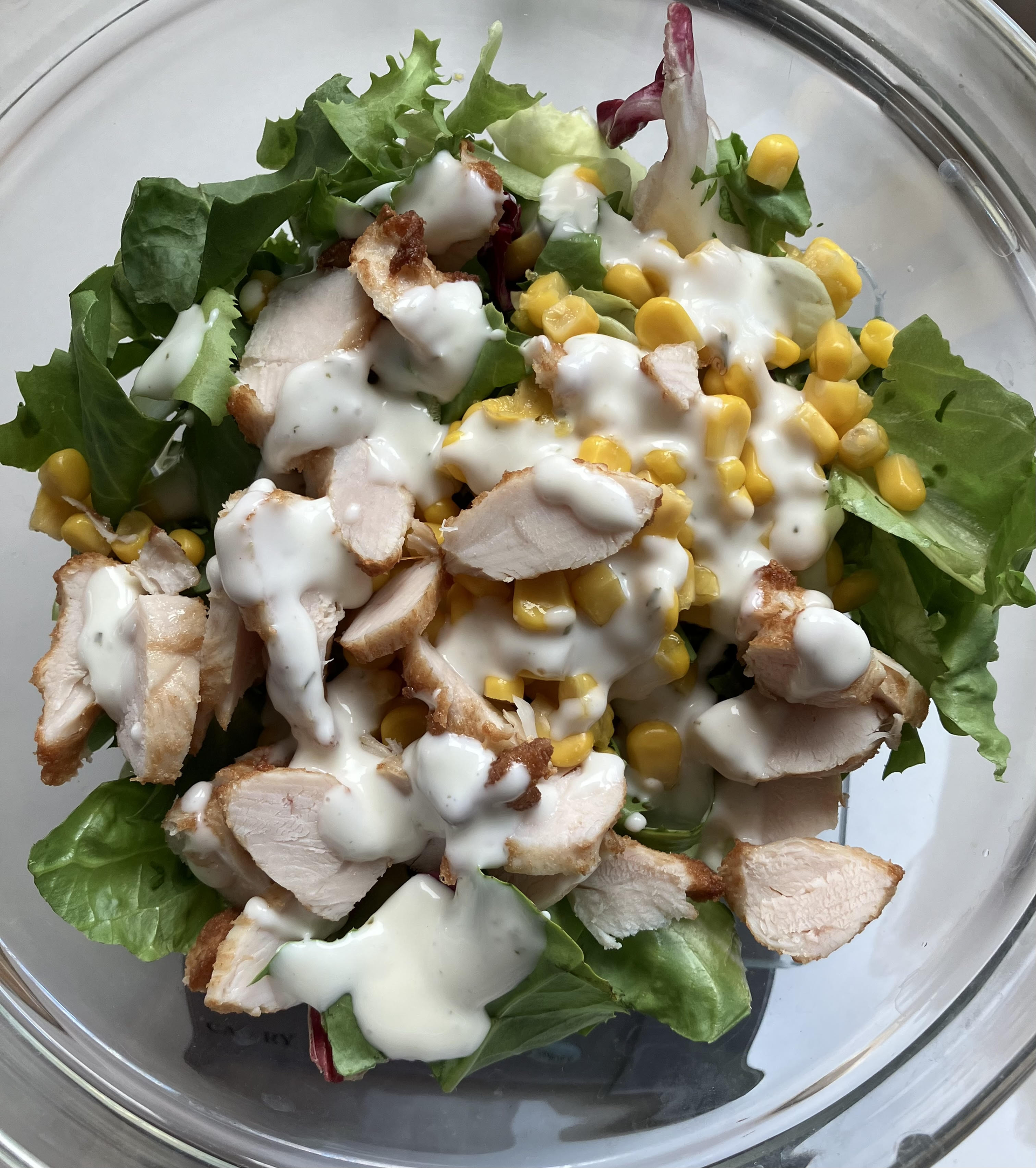 Ein Salat mit Hähnchen, Mais und Salat in einer Glasschüssel