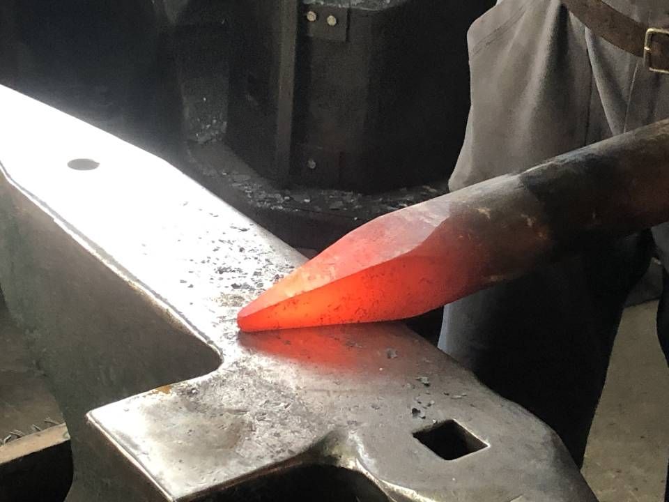 Glühend heisses Metall, das von einem Schmied auf einem Amboss bearbeitet wird.