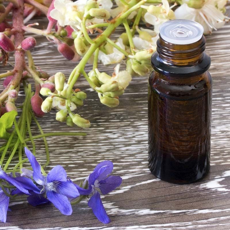 Una botella de aceite esencial está sobre una mesa de madera al lado de flores.