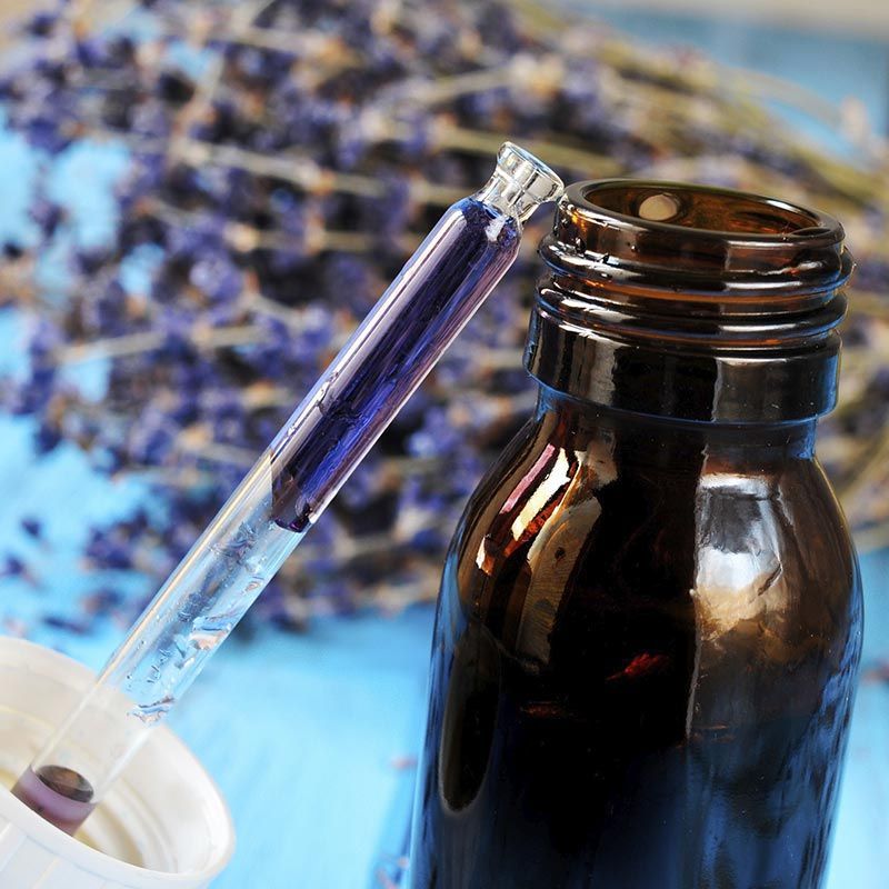 Una botella con una pipeta dentro y flores moradas en el fondo.