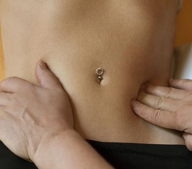 Una mujer con un piercing en el ombligo recibe un masaje de un hombre.