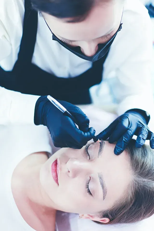 Una mujer se está tatuando las cejas con un tatuador.