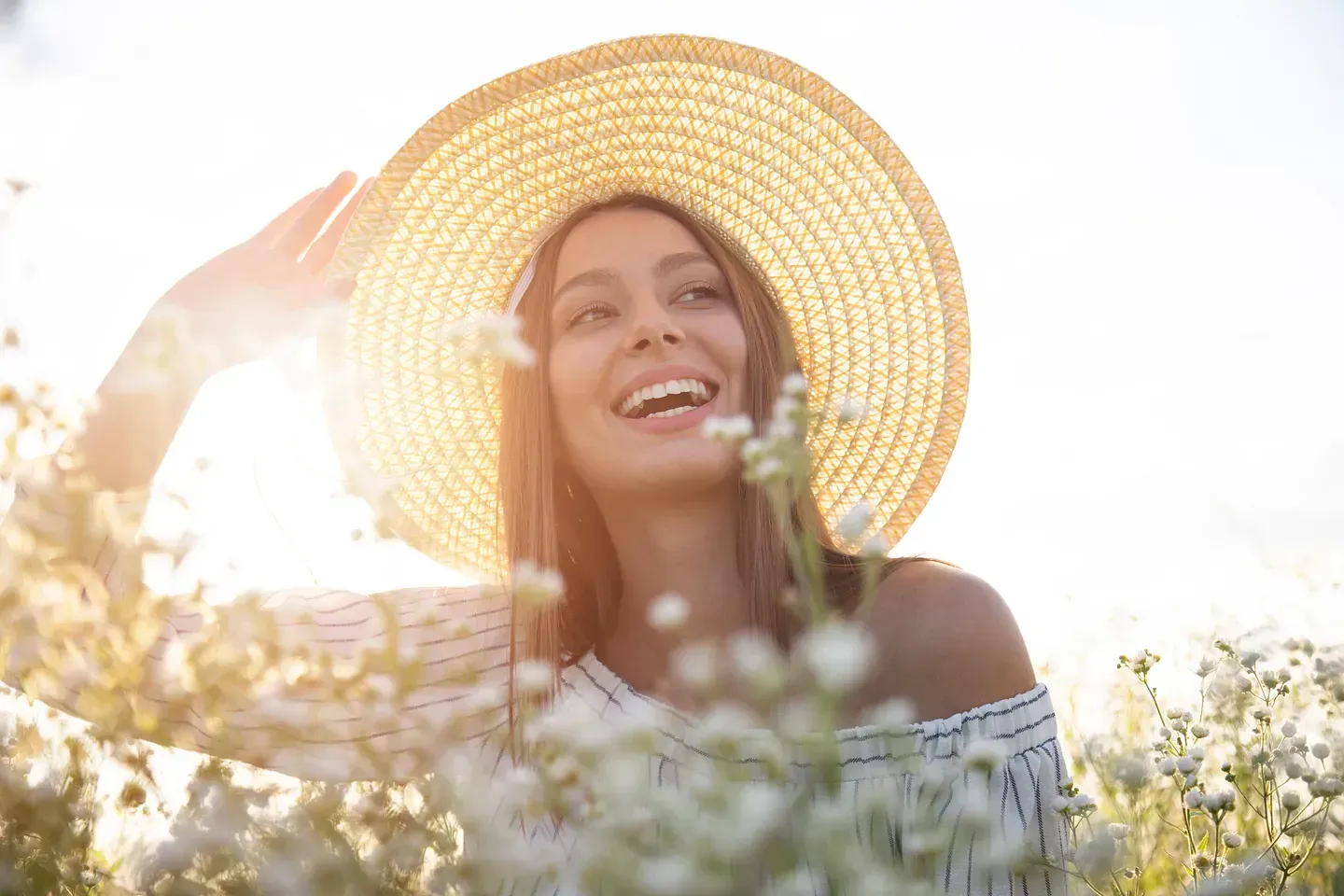Una mujer que lleva un sombrero de paja está parada en un campo de flores.