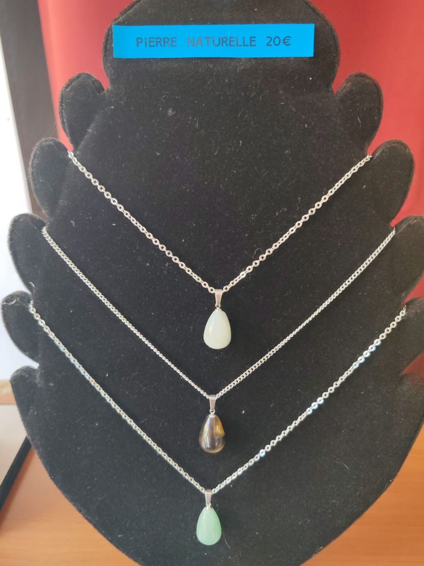 Trois colliers en argent avec des pendentifs en forme de larme présentés sur un présentoir en velours noir.