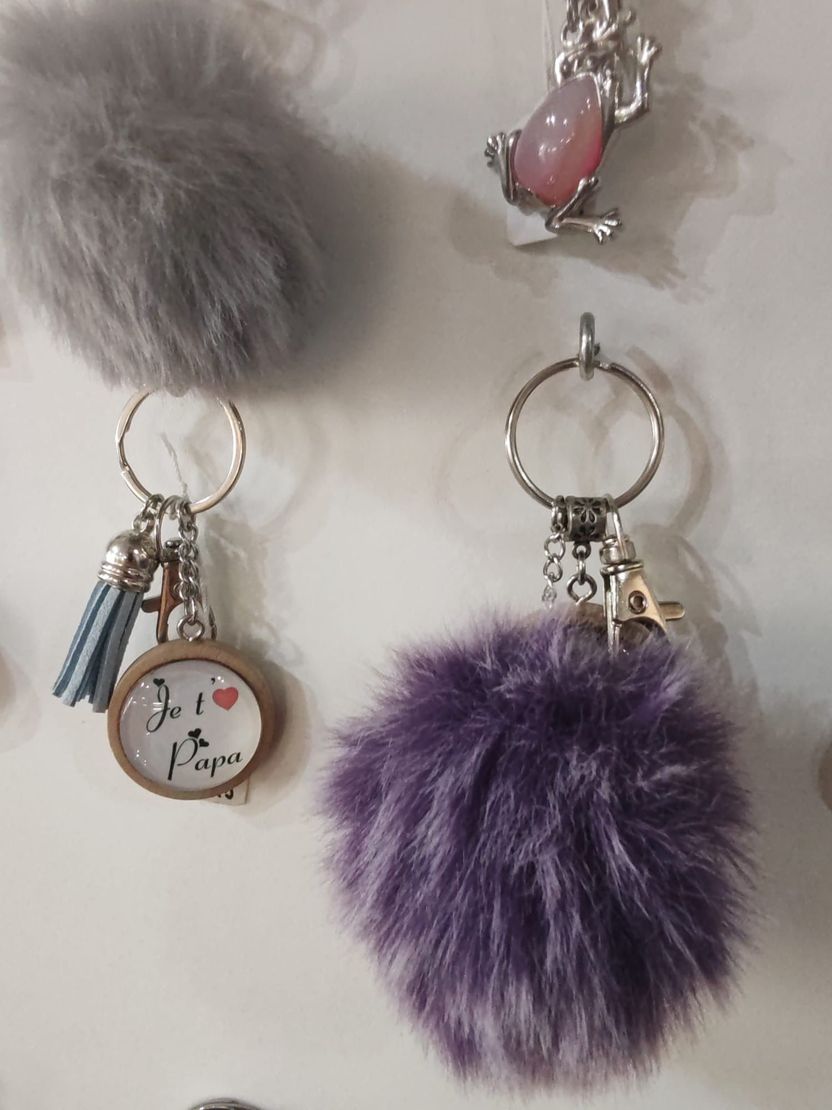 Trois porte-clés avec un pompon duveteux gris, un autre violet et un dernier représentant une grenouille avec une pierre rose.