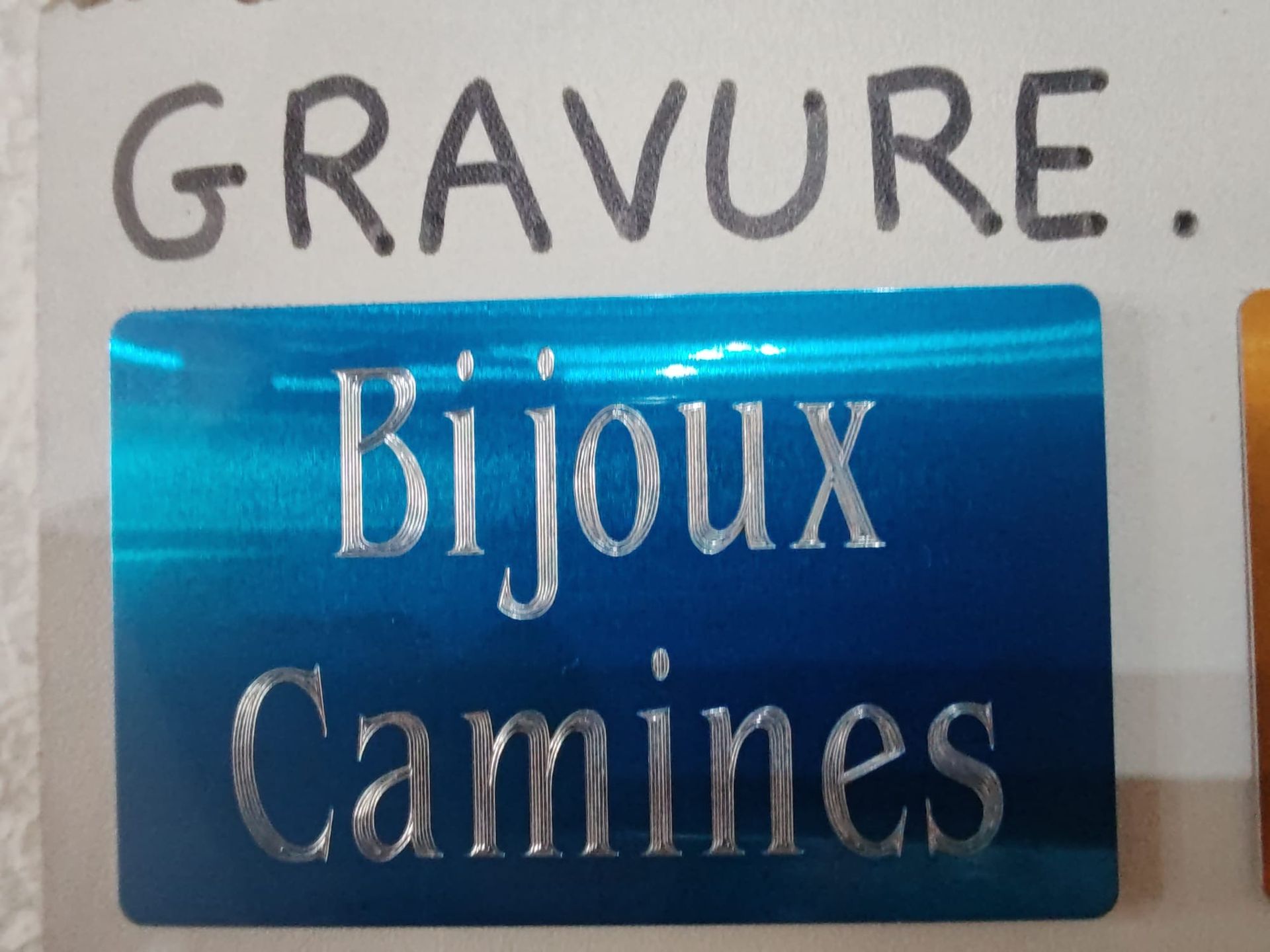 Plaque bleue gravée avec la mention Bijoux Camines sur un socle blanc.