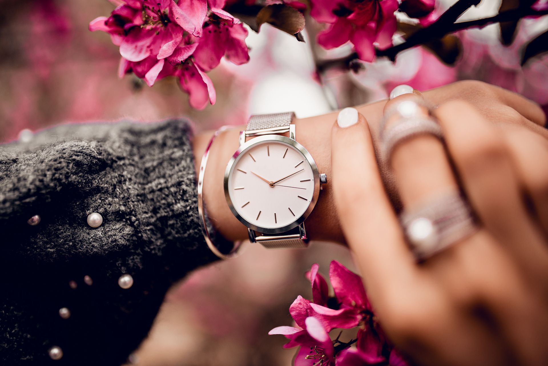 Montre féminine au design minimaliste avec bracelet maille argenté, mise en scène dans un décor floral rose.