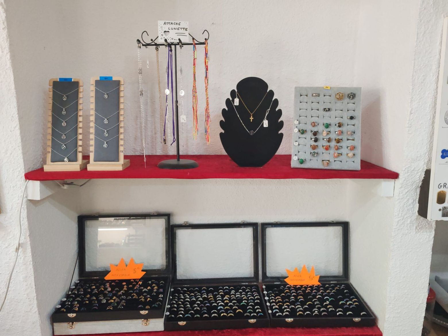 Présentoirs à bijoux sur une étagère rouge, bustes noirs pour colliers et petits plateaux.