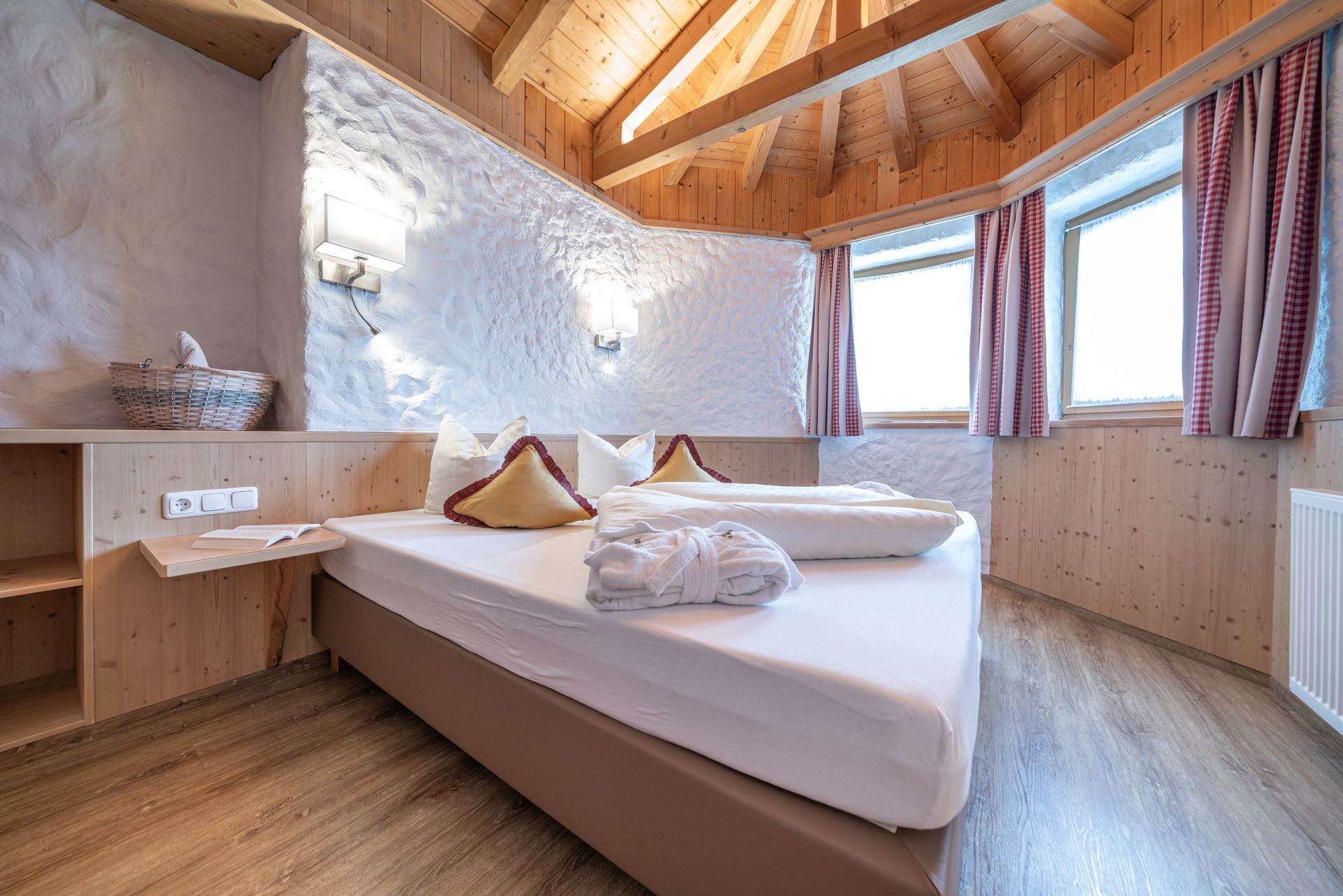 Ein Hotelzimmer mit einem ordentlich gemachten Bett, weiß strukturierten Wänden, Holzvertäfelung und zwei Fenstern.