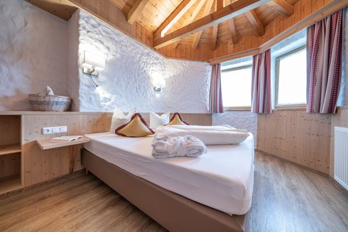 Ein Hotelzimmer mit einem ordentlich gemachten Bett, weiß strukturierten Wänden, Holzvertäfelung und zwei Fenstern.