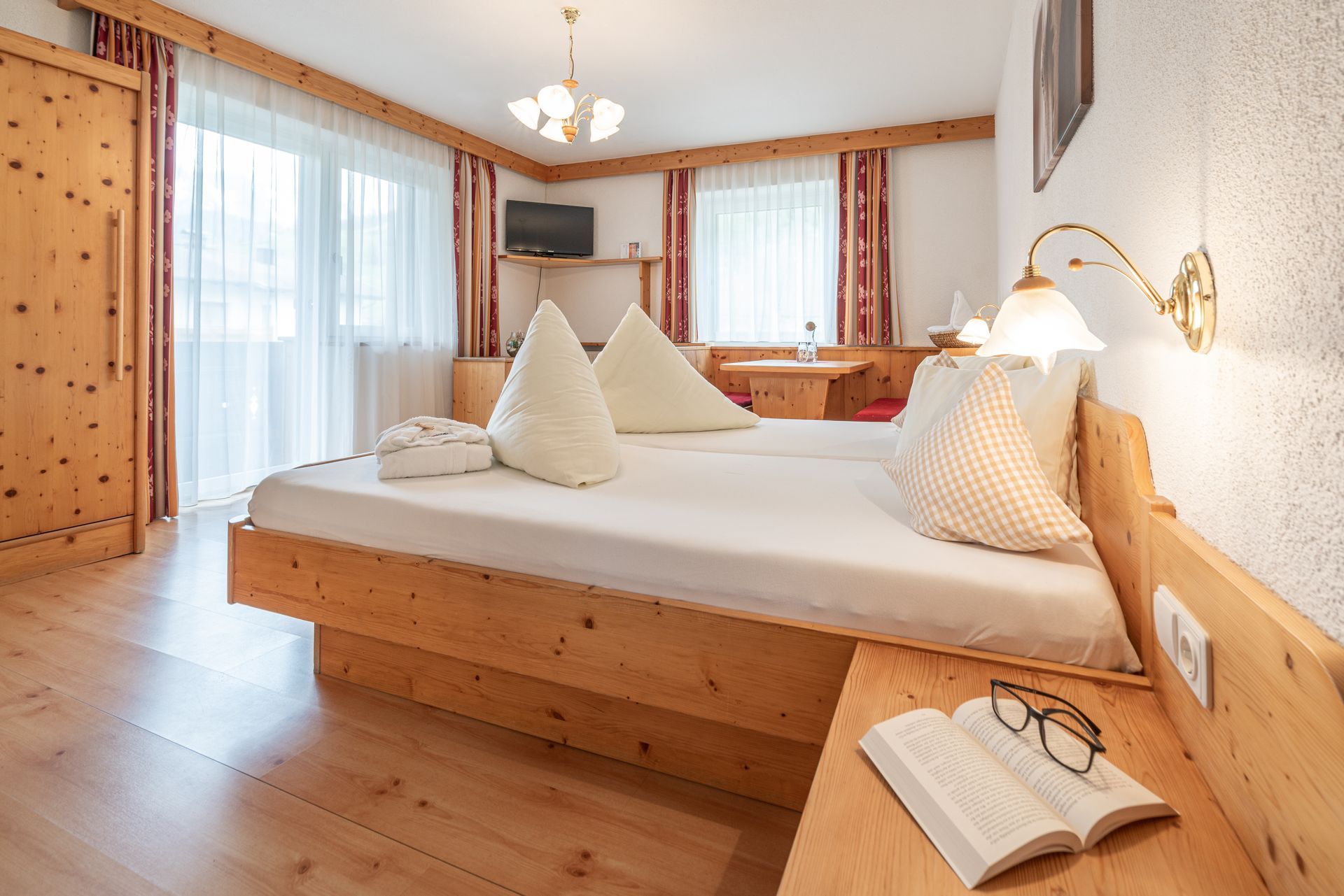 Ein gemütliches Hotelzimmer im alpinen Stil mit zwei Betten, Holzvertäfelung, bodentiefen Fenstern.