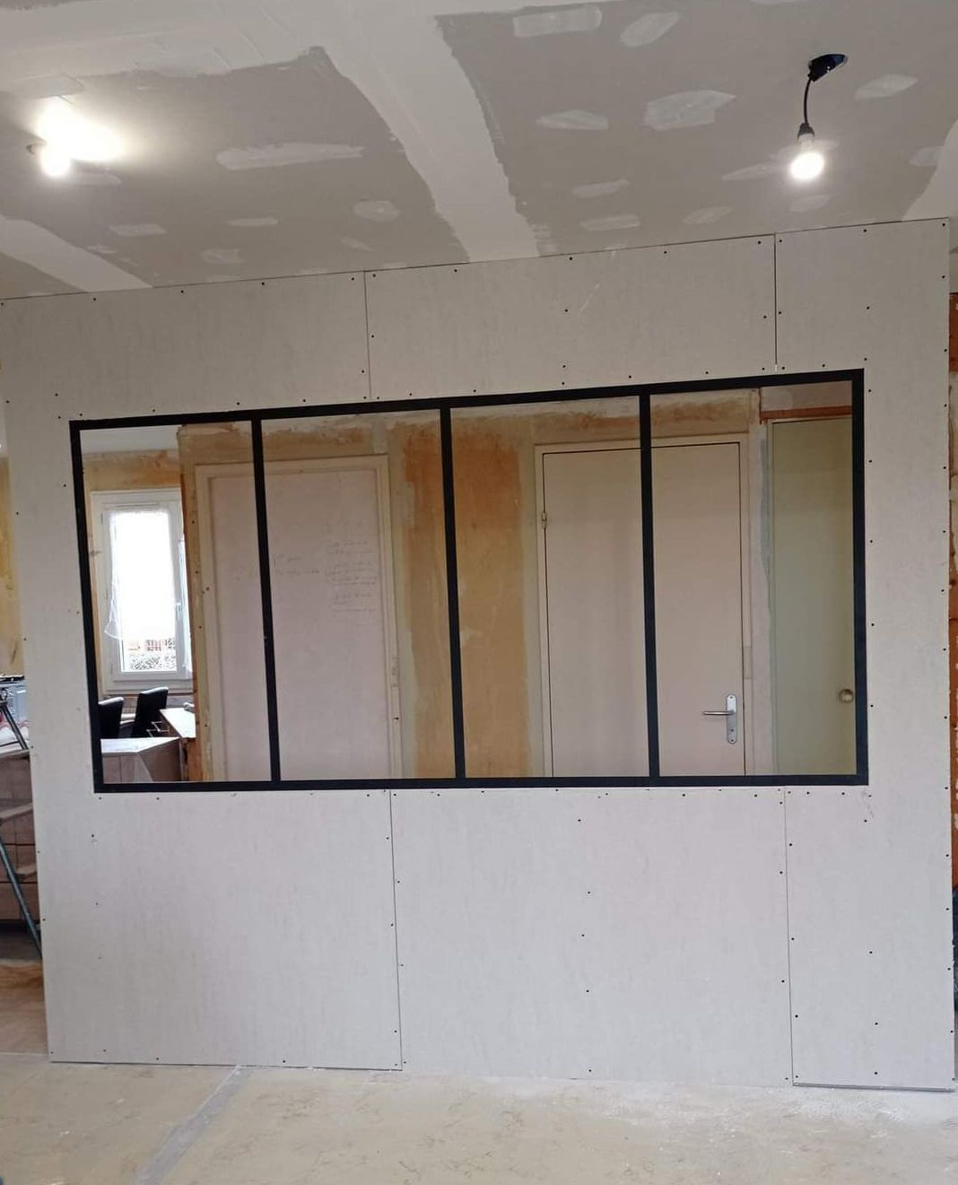 Mur recouvert de plaques de plâtre avec fenêtres à cadre noir ; travaux intérieurs en cours