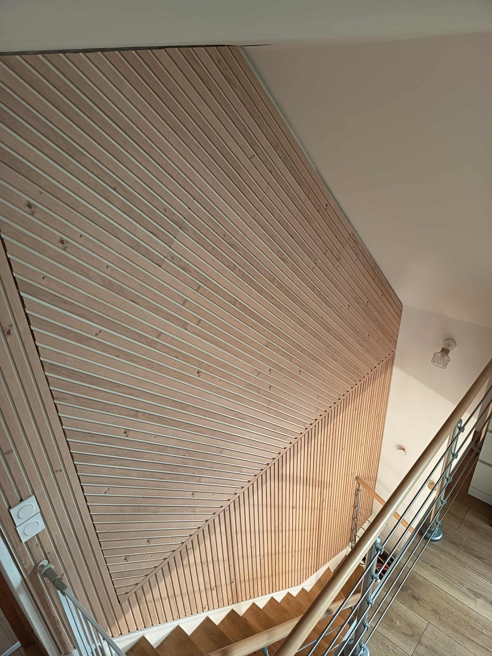 Lambris en bois à lignes obliques, jouxtant un escalier avec une rampe en métal