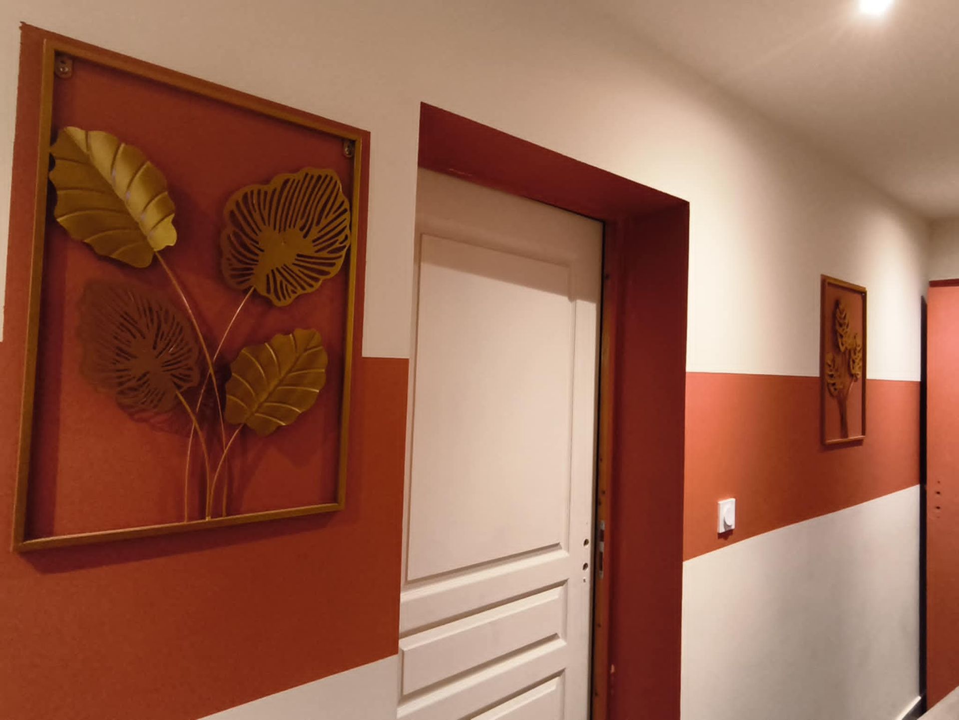 Couloir aux murs, porte et décorations murales en terre cuite et blancs, ornés de feuilles d'or