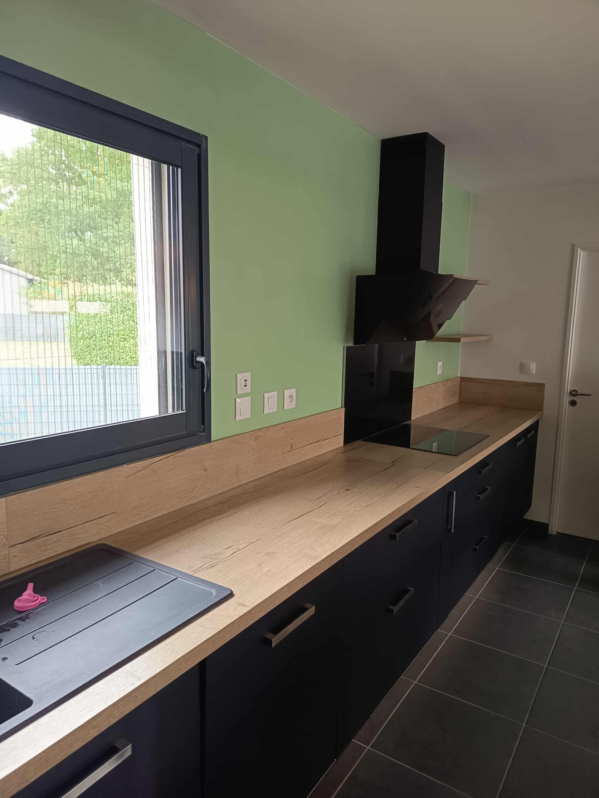 Cuisine avec placards noirs, comptoirs en bois clair, mur vert et hotte noire