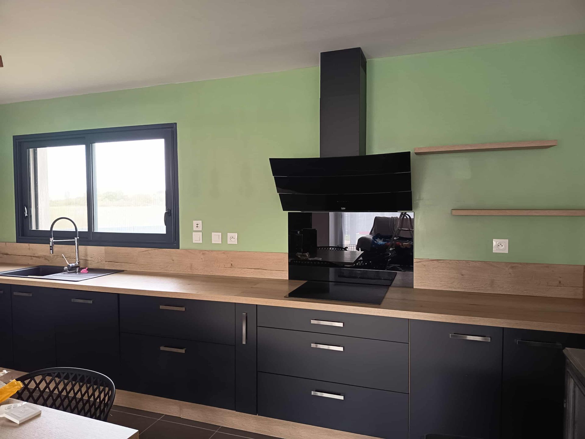 Cuisine avec placards noirs, murs verts et hotte noire