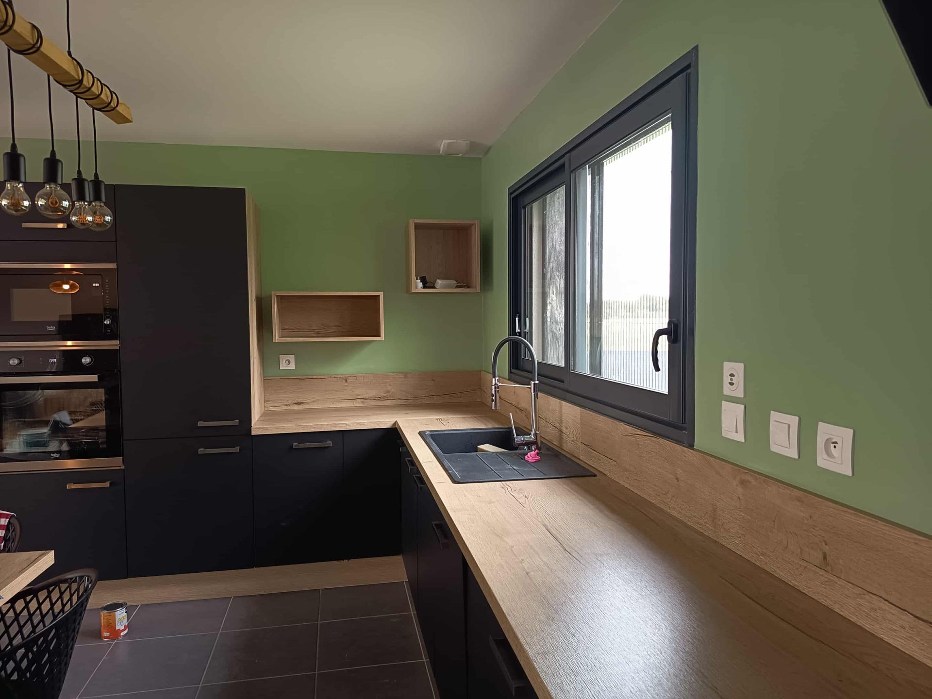 Une cuisine moderne avec des placards noirs, un plan de travail en bois et des murs verts