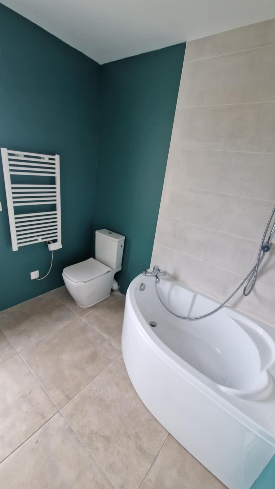 Salle de bains avec mur turquoise, toilettes blanches, sèche-serviettes chauffant et baignoire incurvée