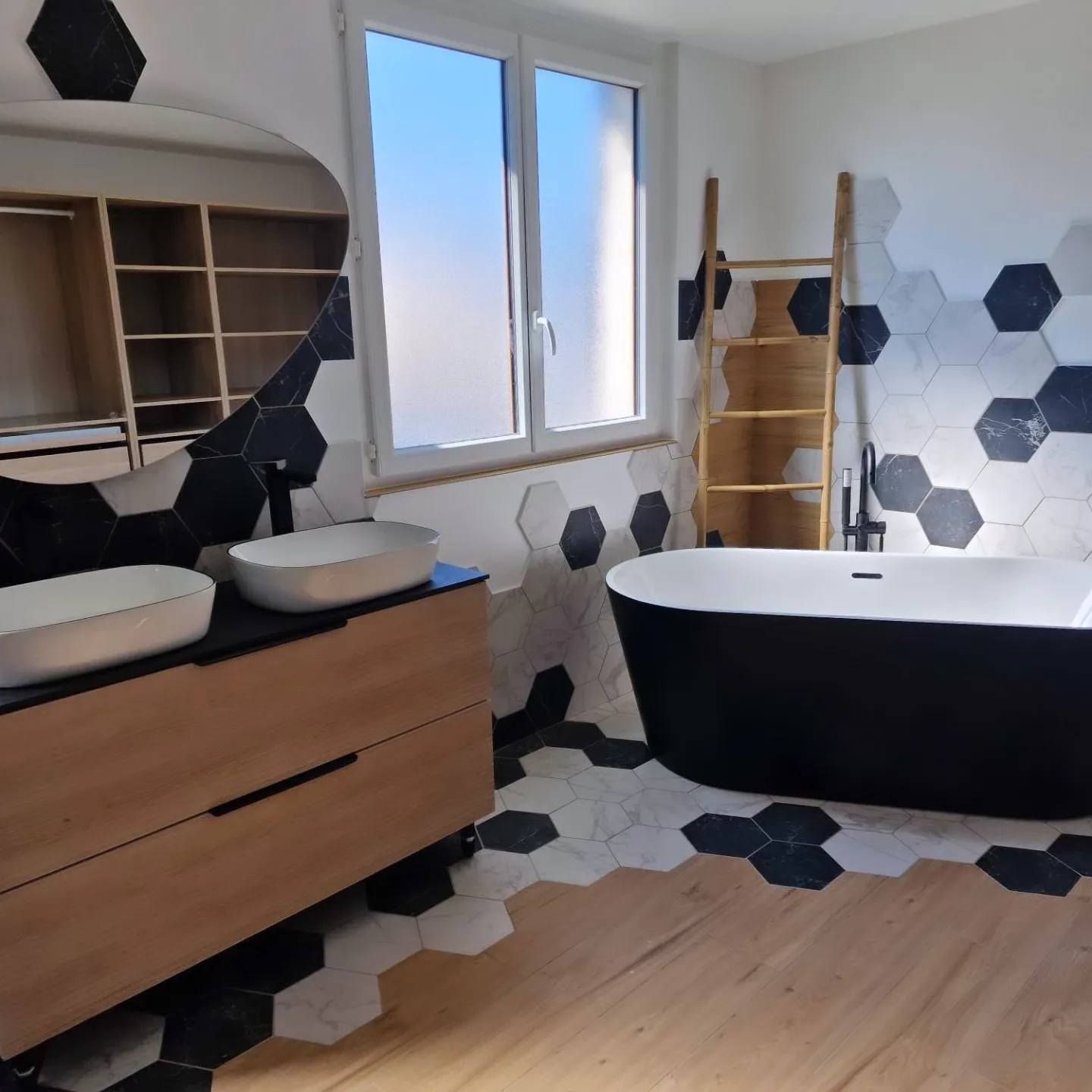 Salle de bains moderne avec carrelage hexagonal noir et blanc, meuble-lavabo en bois et baignoire noire sur pieds