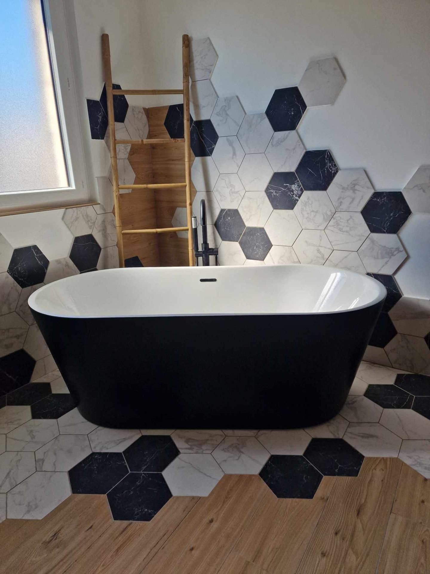 Baignoire îlot noire dans une salle de bains carrelée de carreaux hexagonaux et équipée d'une échelle en bois