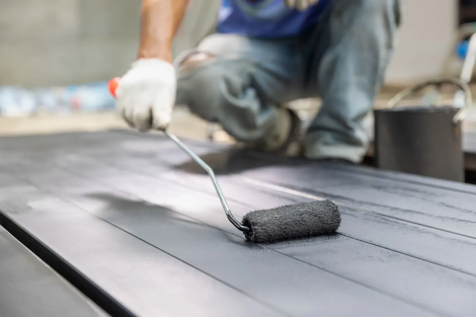 Personne utilisant un rouleau à peinture pour appliquer de la peinture grise sur une surface métallique.