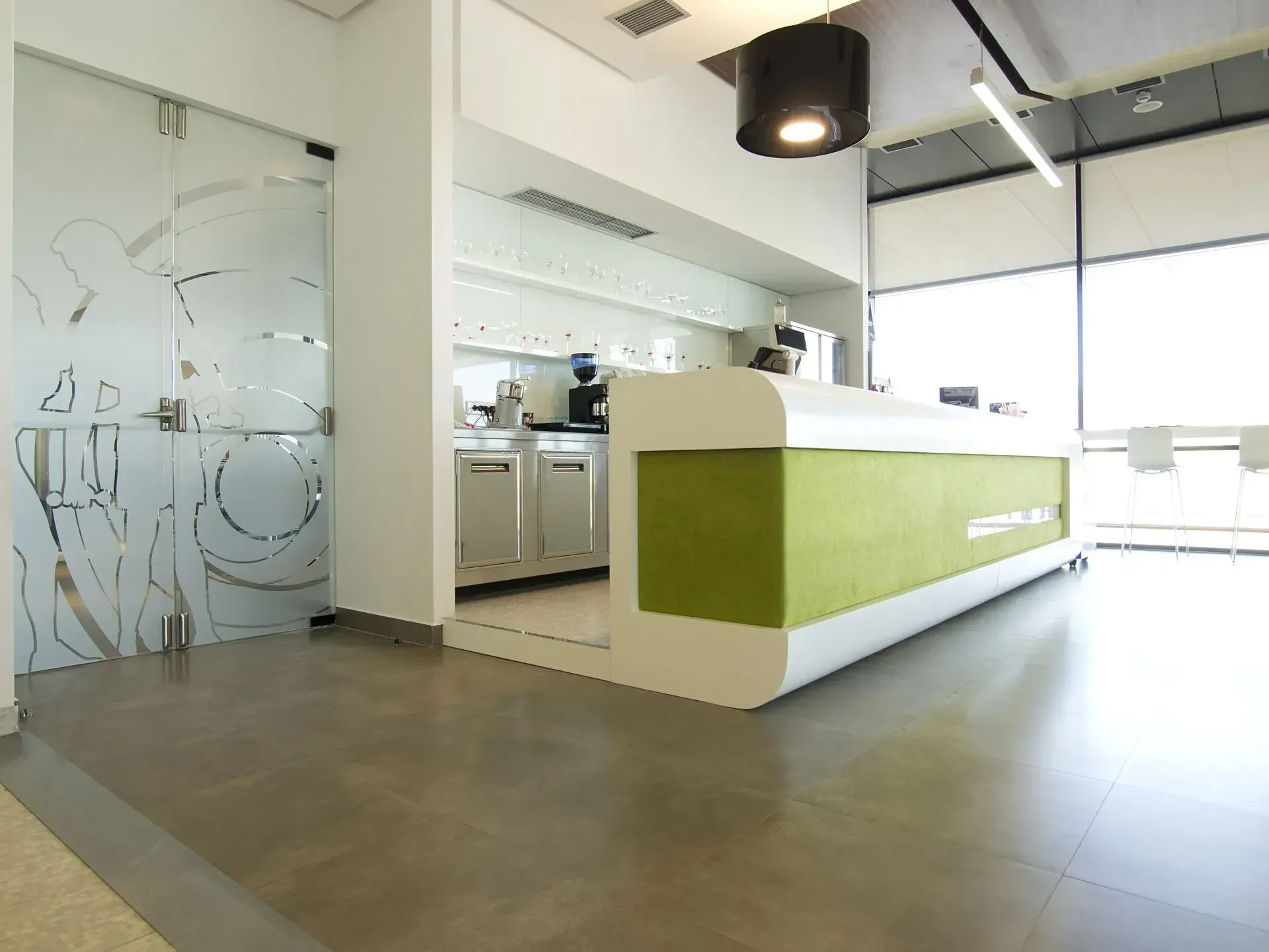 Espace de réception de bureau moderne avec comptoir vert et blanc, porte en verre dépoli et grandes fenêtres.